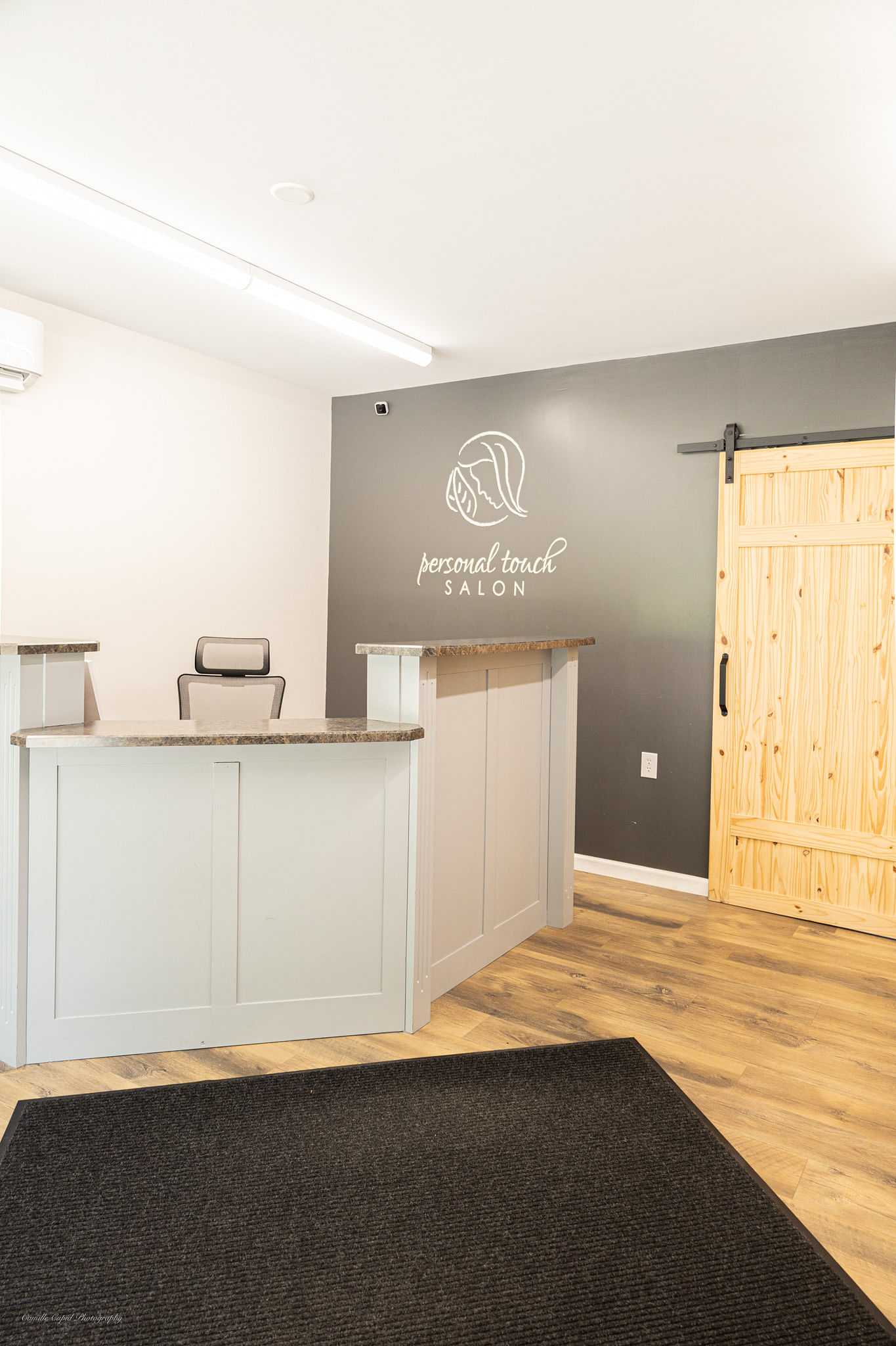 Reception area of a salon with a logo on the wall and wooden sliding door on the right.